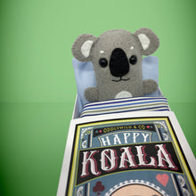 Load image into Gallery viewer, Handmade from felt this mini grey koala toy stands 110mm high and is perfect for your kids to that with them on their travels and adventures. Your little friend is small enough to fit in a pocket and comes with its own matchbox and bedding.